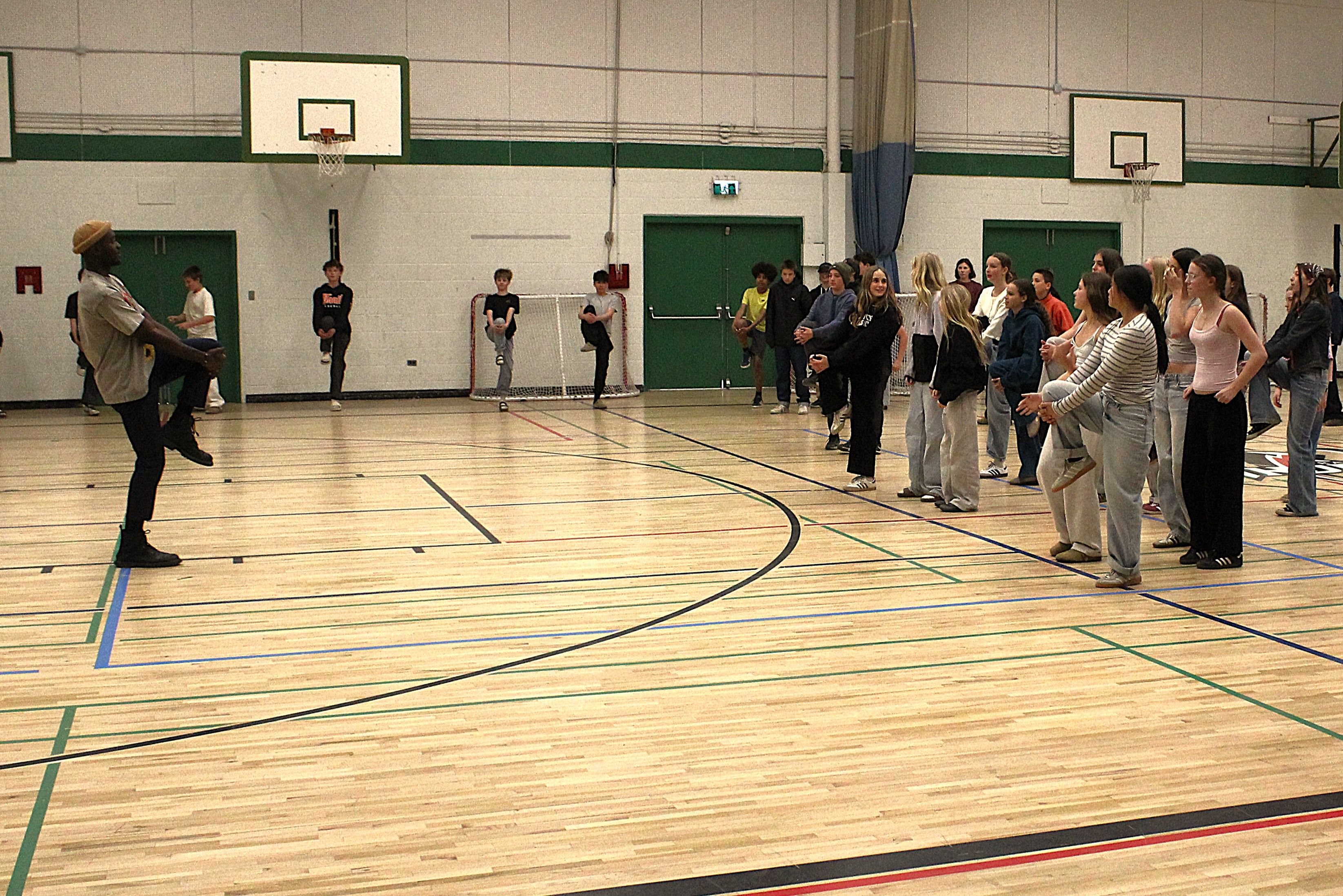 Students and facilitator in a collective stretching and movement exercise in a gymnasium