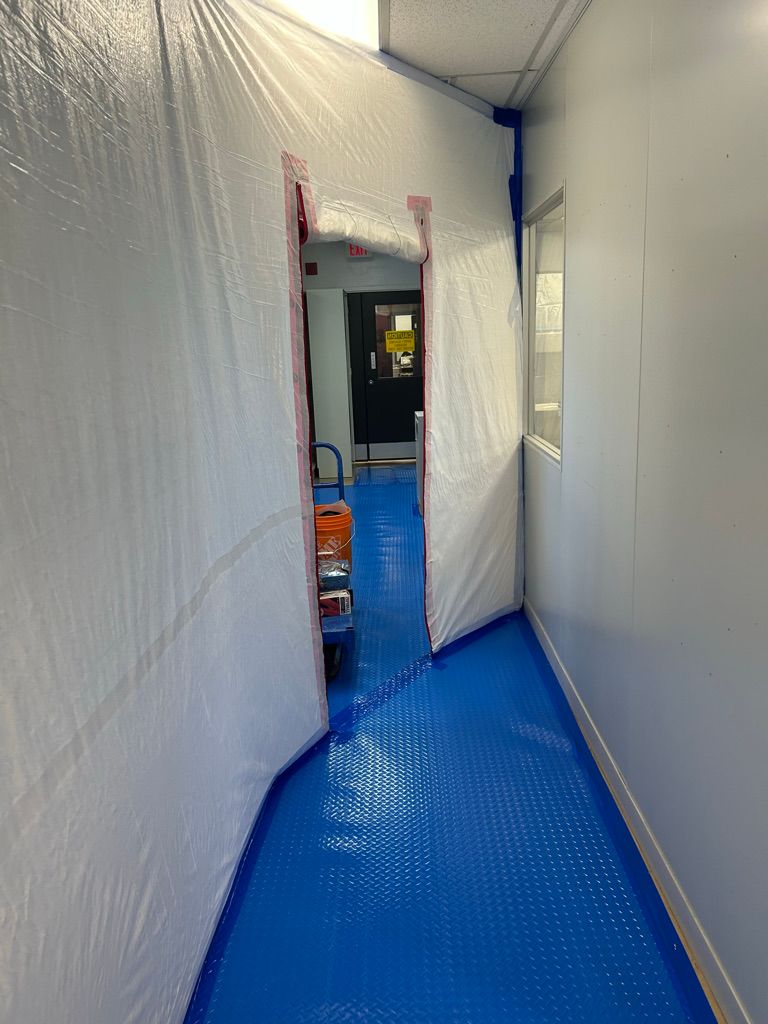 Newly installed bright blue seamless floor in a pharmaceutical corridor with containment sheeting and yellow caution signage in place during installation