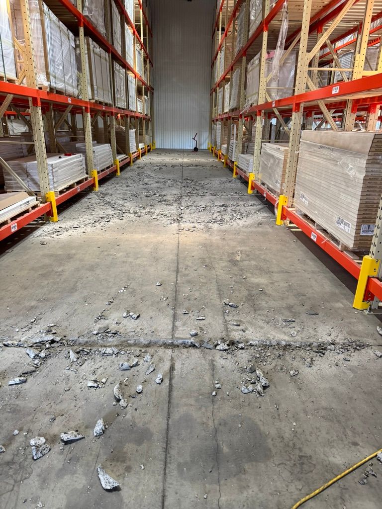 Warehouse aisle before-shot showing debris and deteriorated concrete flooring alongside stocked shelving