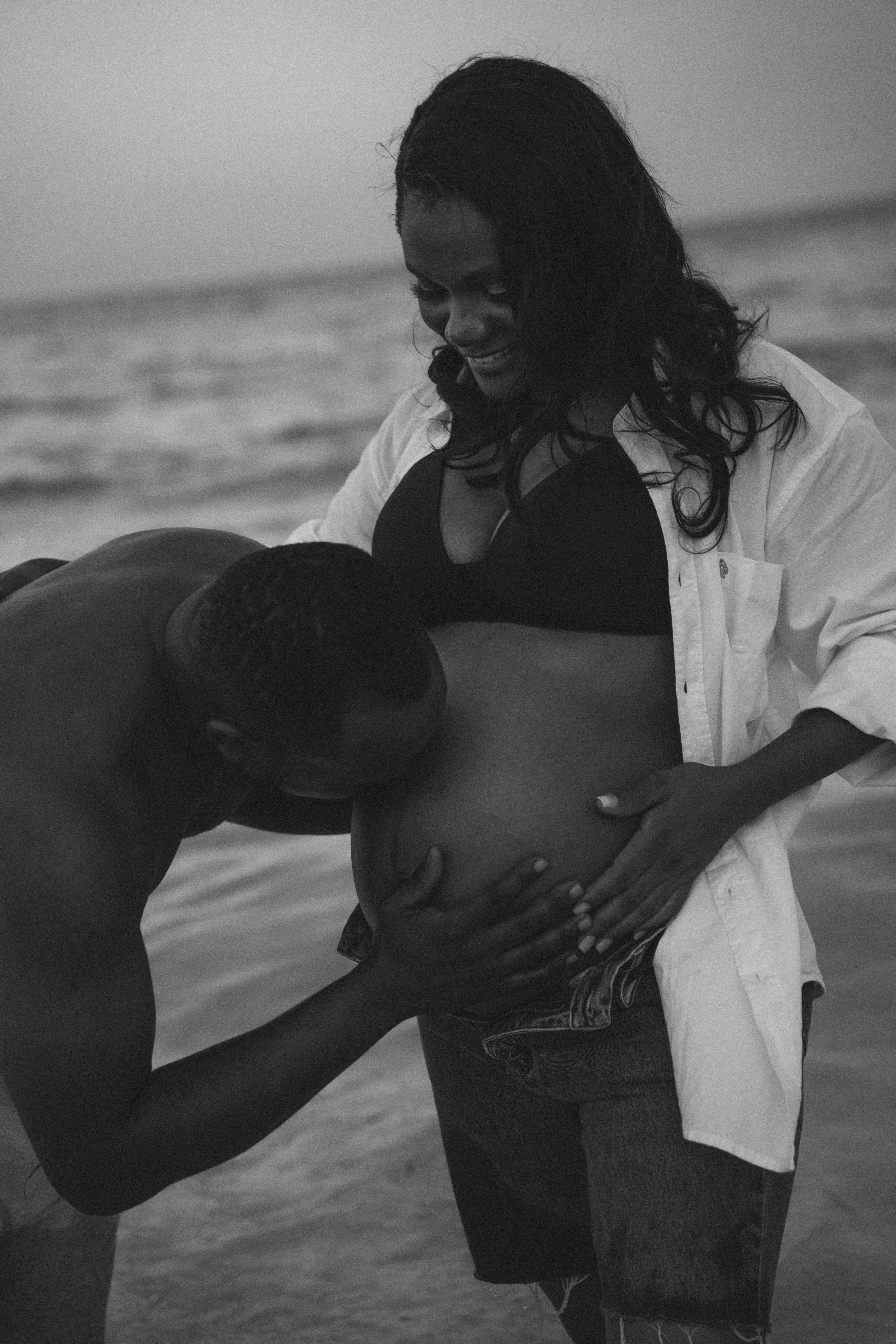 Man kissing pregnant belly in shallow ocean water - maternity photoshoot Zanzibar