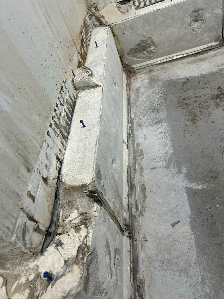 Close-up of chipped and deteriorated concrete corner with anchoring screws before cove base repair