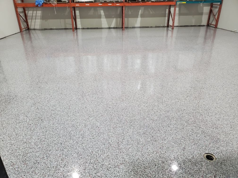 Warehouse utility room with highly reflective speckled epoxy floor featuring a recessed drain and shelving