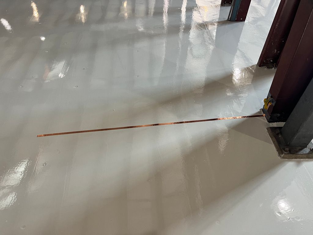 Shiny smooth light gray ESD floor with copper grounding strip and two vertical metal structural beams