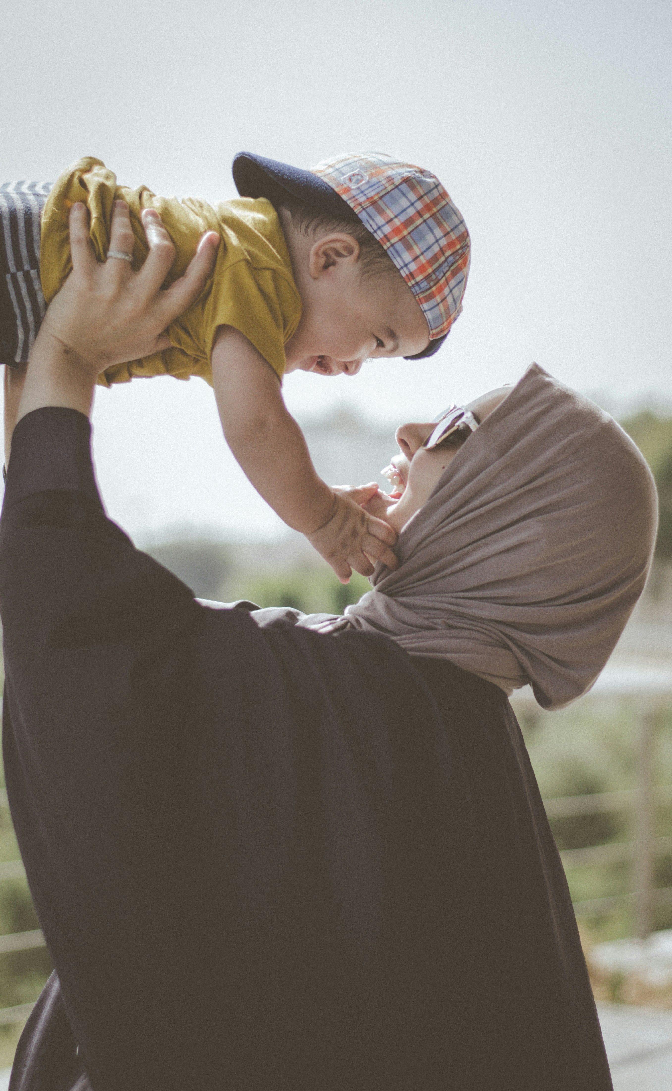 Mother in hijab joyfully holding her baby up in the air
