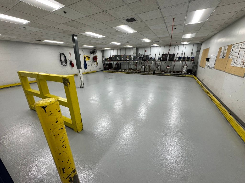 Large clean manufacturing facility with smooth light grey epoxy floor, yellow safety barriers and control panel wall