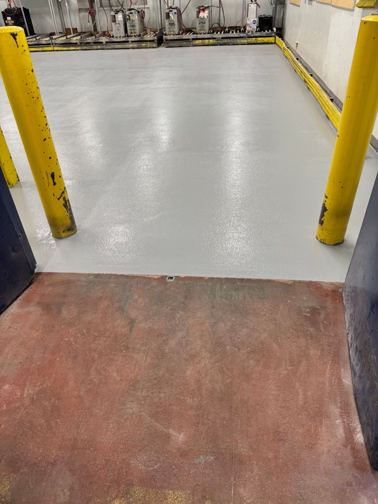 Floor transition from worn surface to new smooth grey epoxy with yellow safety bollards and industrial equipment
