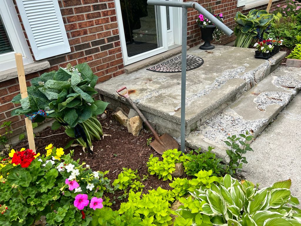 Concrete front porch with two steps and metal railing before restoration — brick house entrance with garden