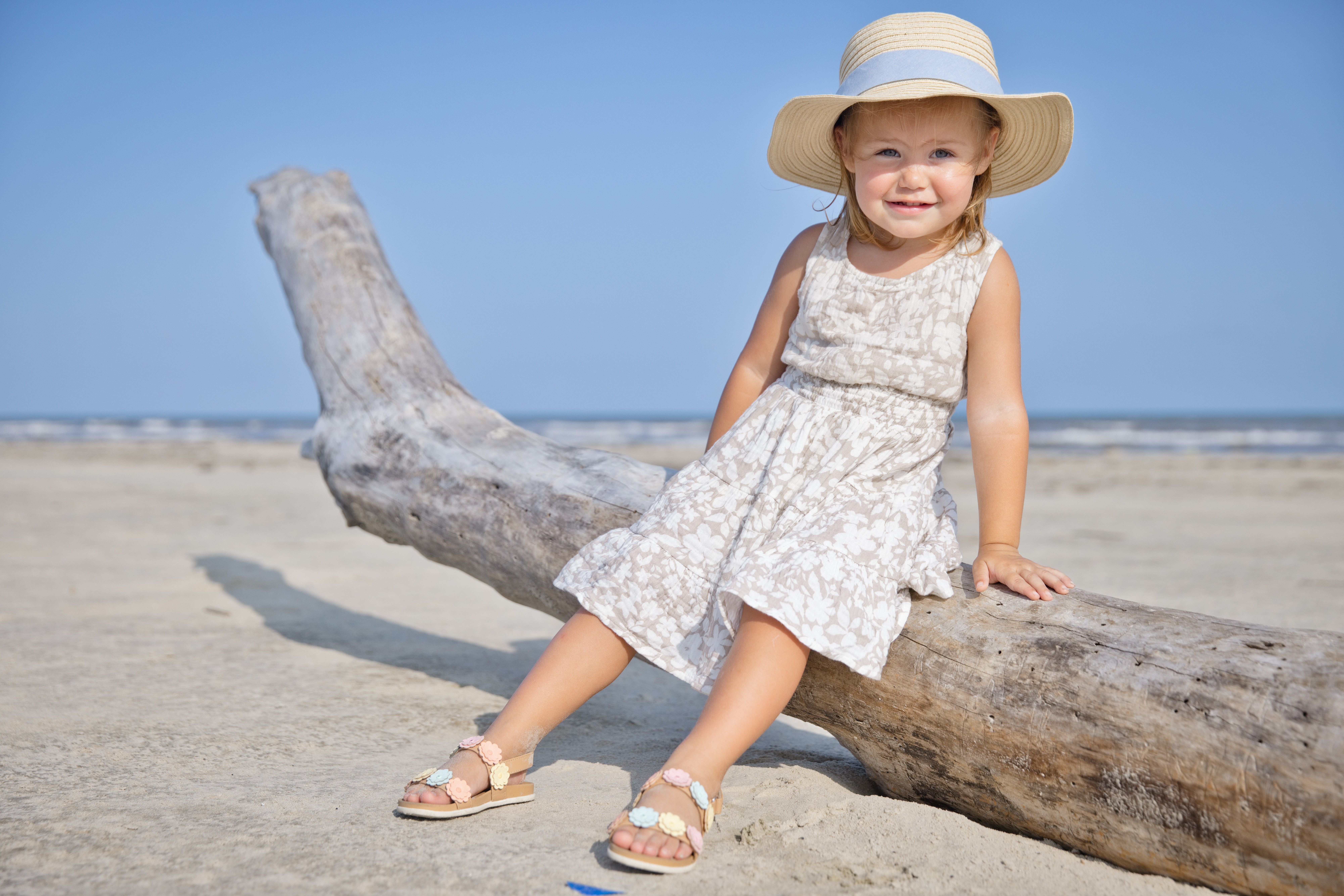 Little girl sitting on driftwood wearing a sunhat