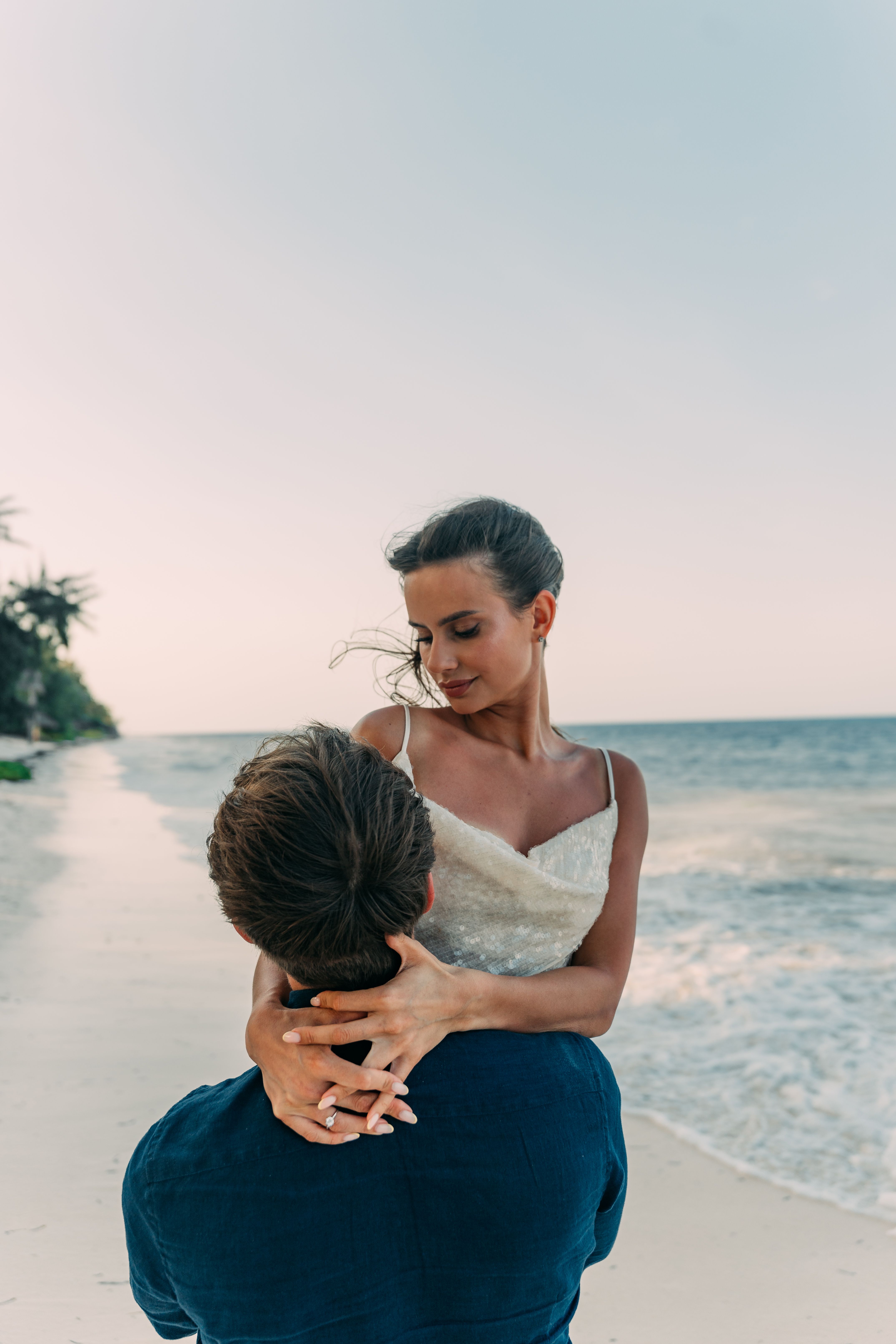 Couple embracing on Zanzibar beach - woman in white dress, man in dark blue shirt