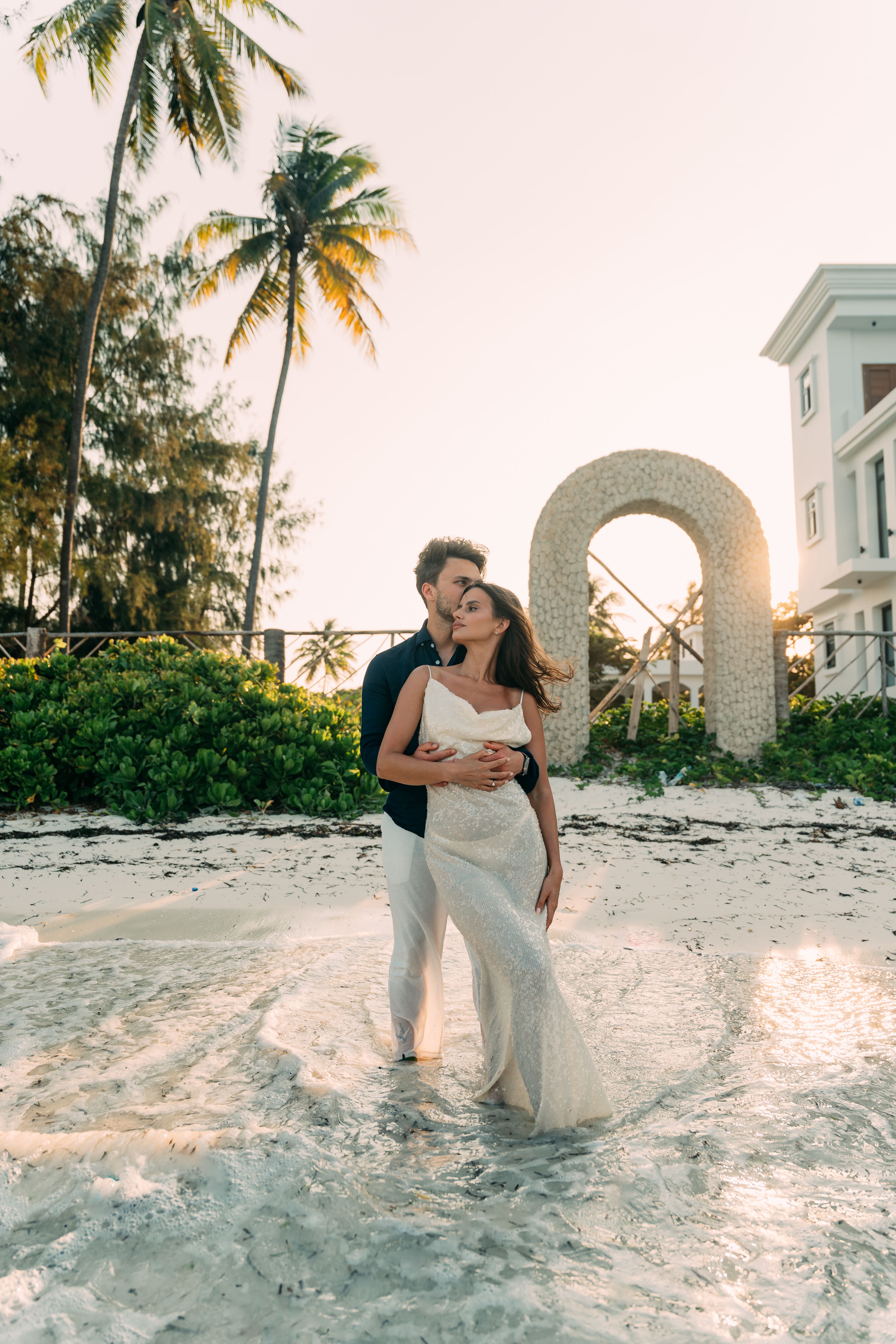 Couple standing by stone arch on Zanzibar beach at golden hour