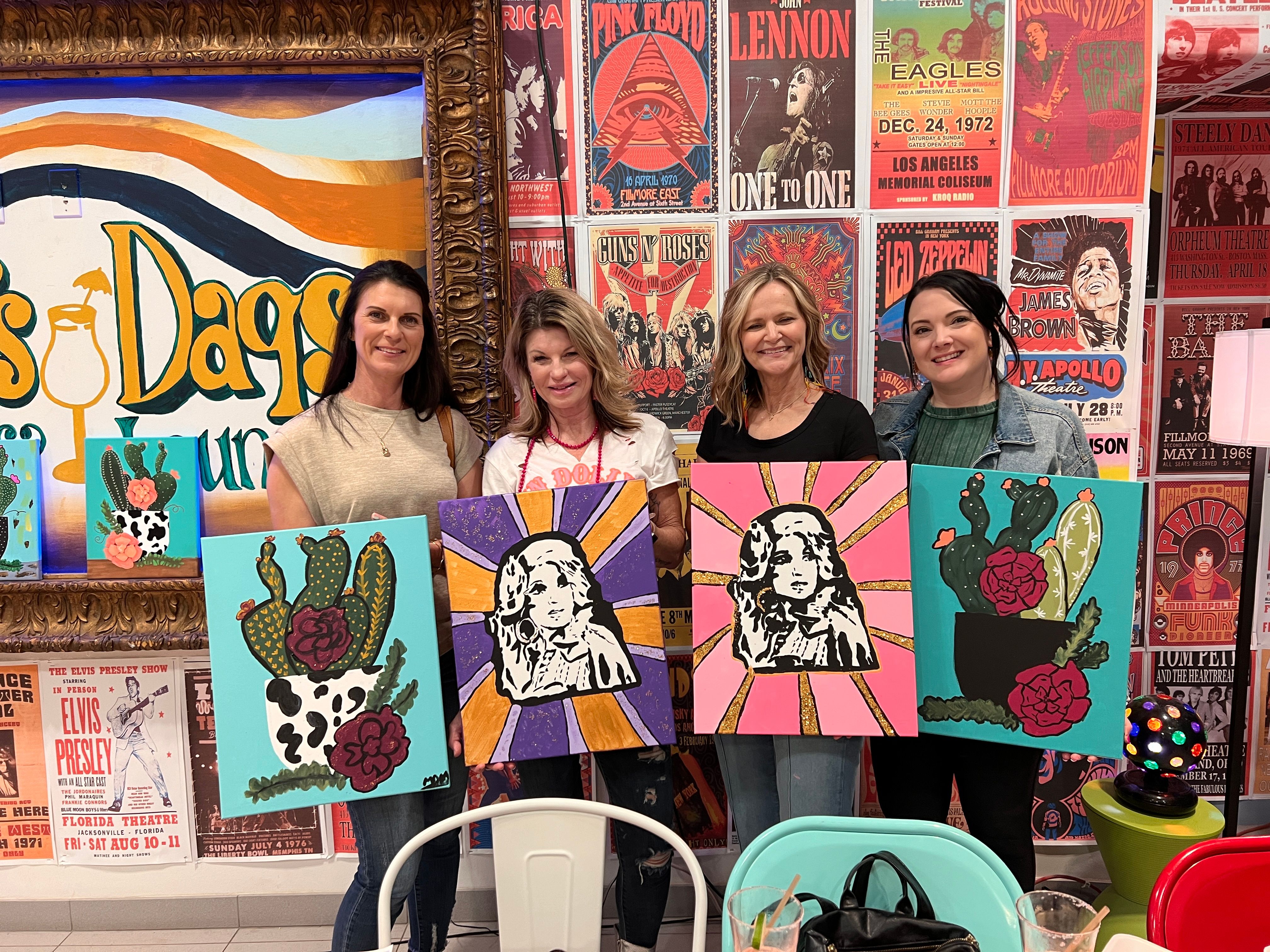 Women holding their finished paintings at an adult paint party