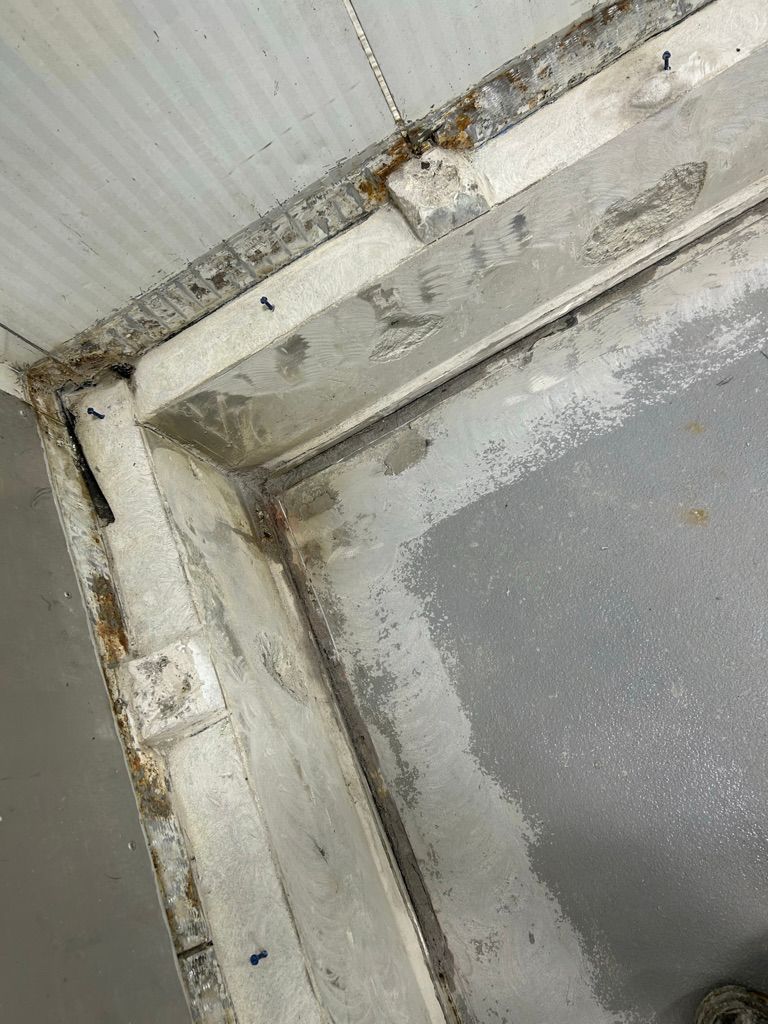 Close-up of corrugated metal panel and cove base with rough polymer repair and visible fasteners before finishing