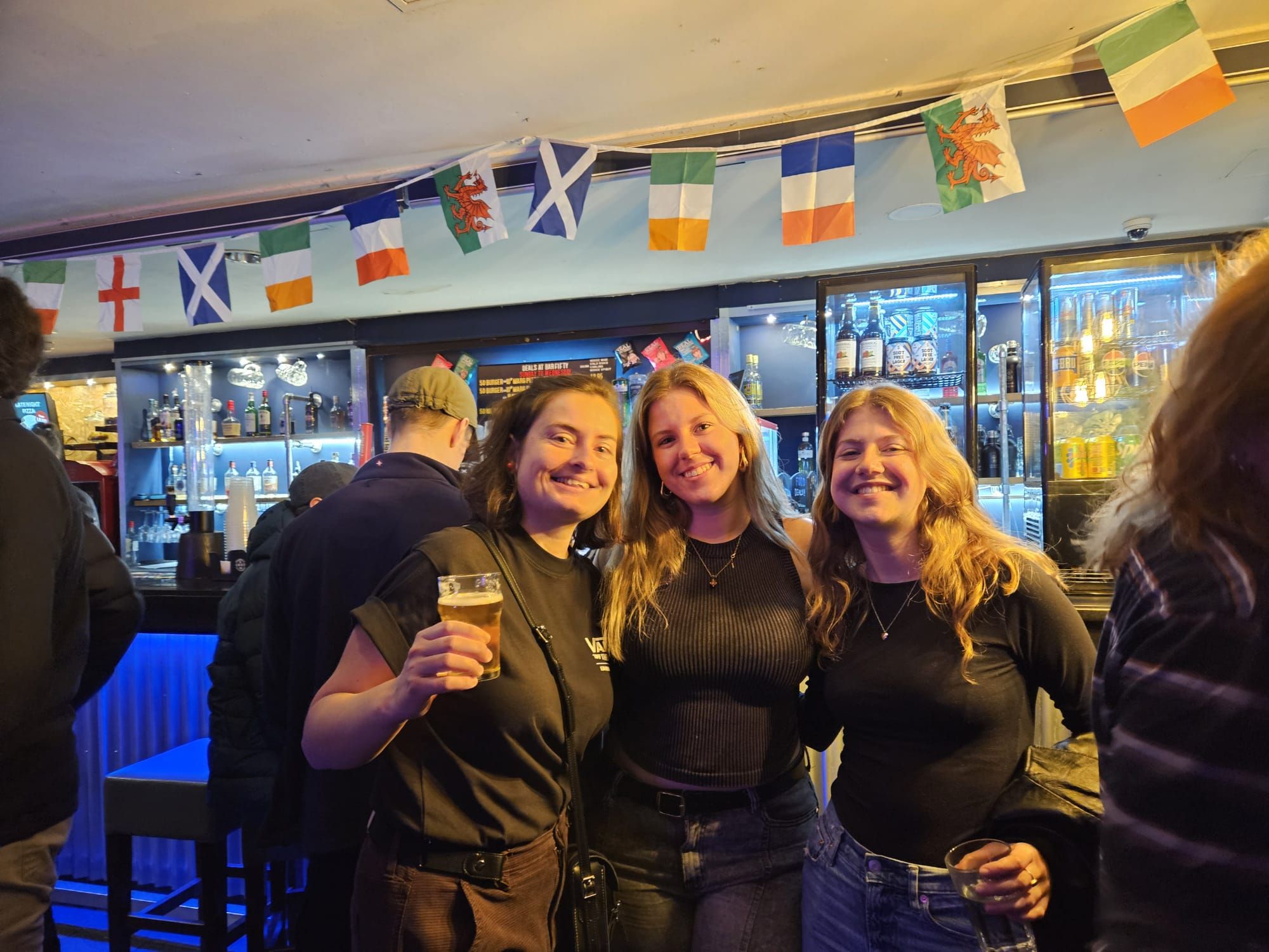 Three women smiling with cocktails at an Ebrius Glasgow pub crawl venue on a Saturday night out