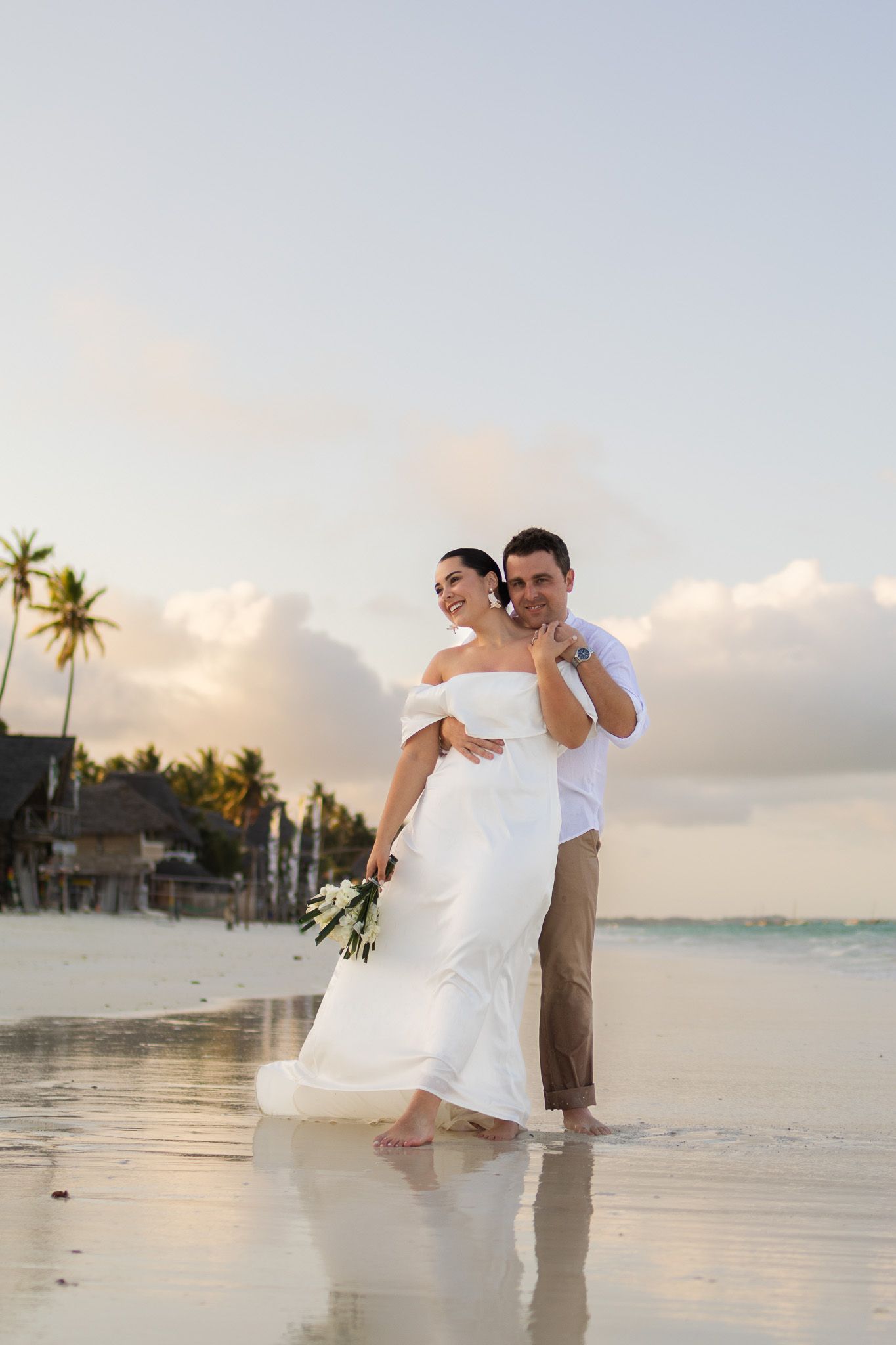 Couple embracing on beach with white bouquet and palm trees