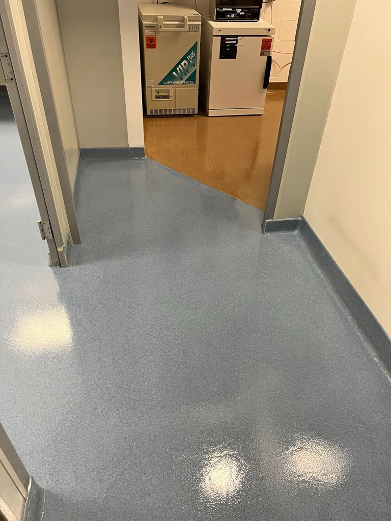 Transition between new shiny blue seamless floor and existing flooring in a pharmaceutical facility with sterile lab equipment visible through the doorway