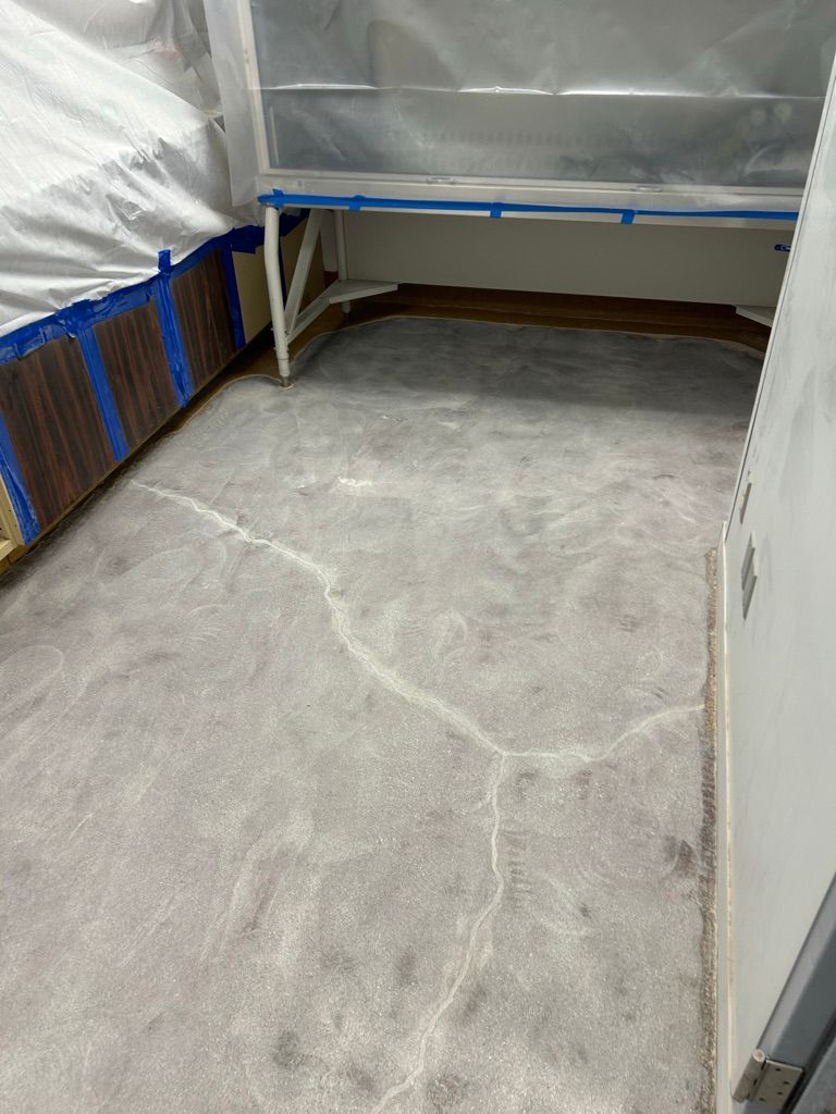 Before view of a deteriorated pharmaceutical floor with uneven cracked surface, walls protected with sheeting in preparation for epoxy application