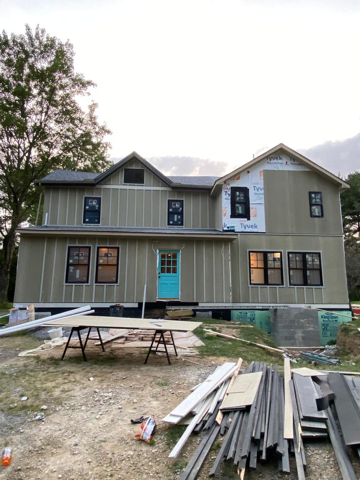 New construction home with beige board and batten siding and turquoise front door