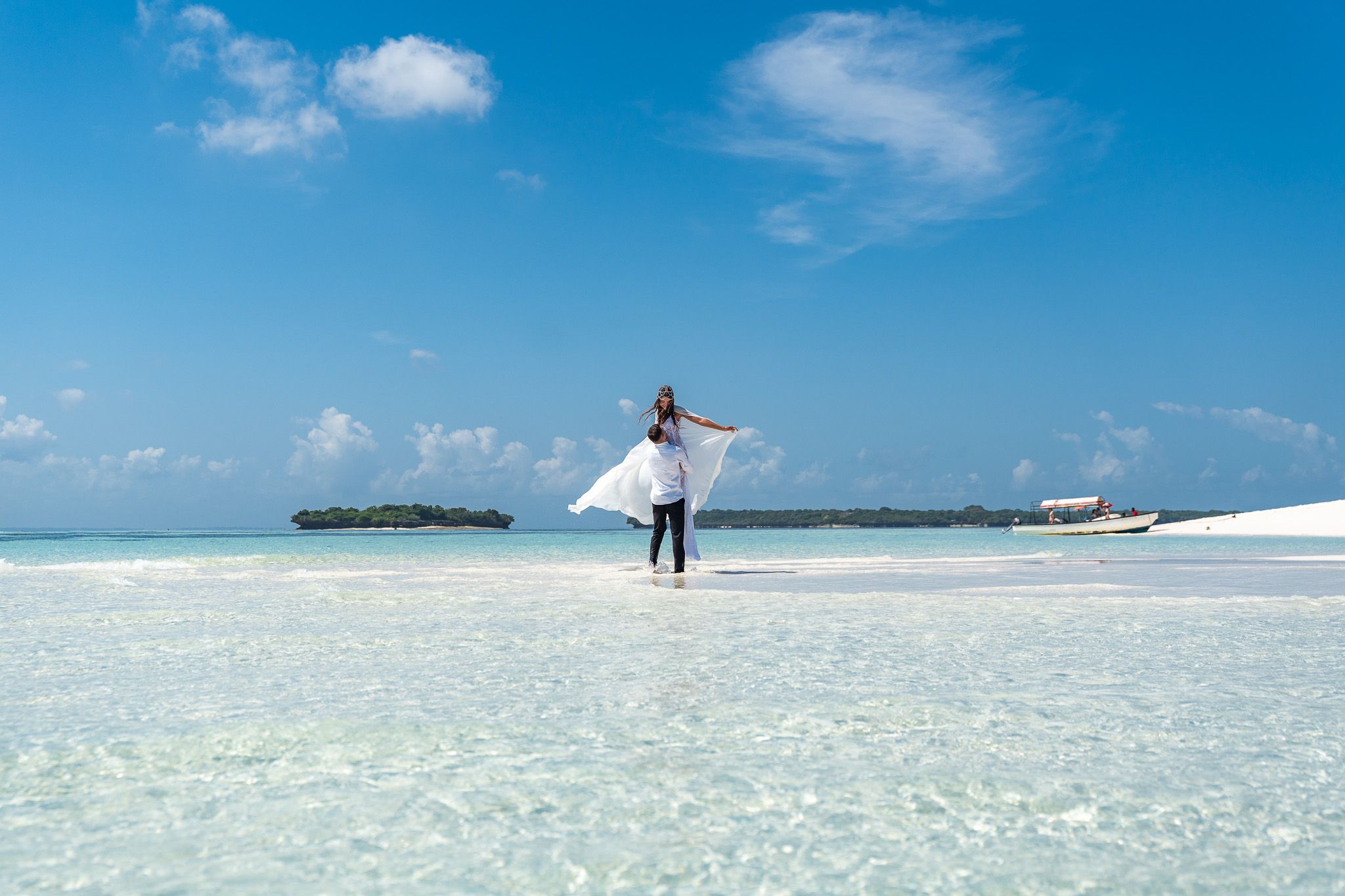 Man lifting woman in shallow turquoise water on Zanzibar sandbank