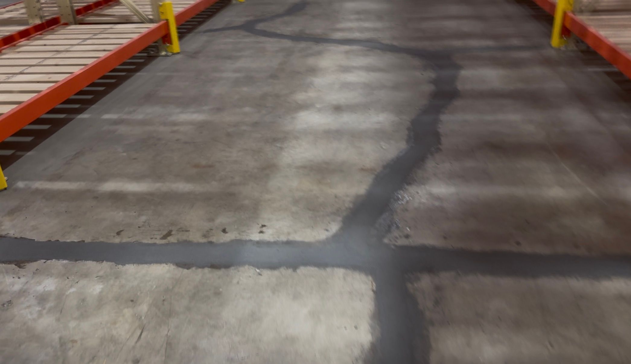 Warehouse aisle before-shot showing concrete floor with filled cracks between red storage racks