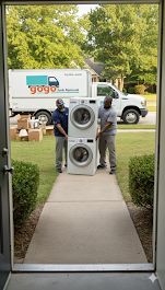GoGo Junk Removal technician moving stacked washer and dryer unit on dolly outside residential home