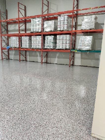 Warehouse storage area with speckled epoxy floor and red metal shelving stocked with product