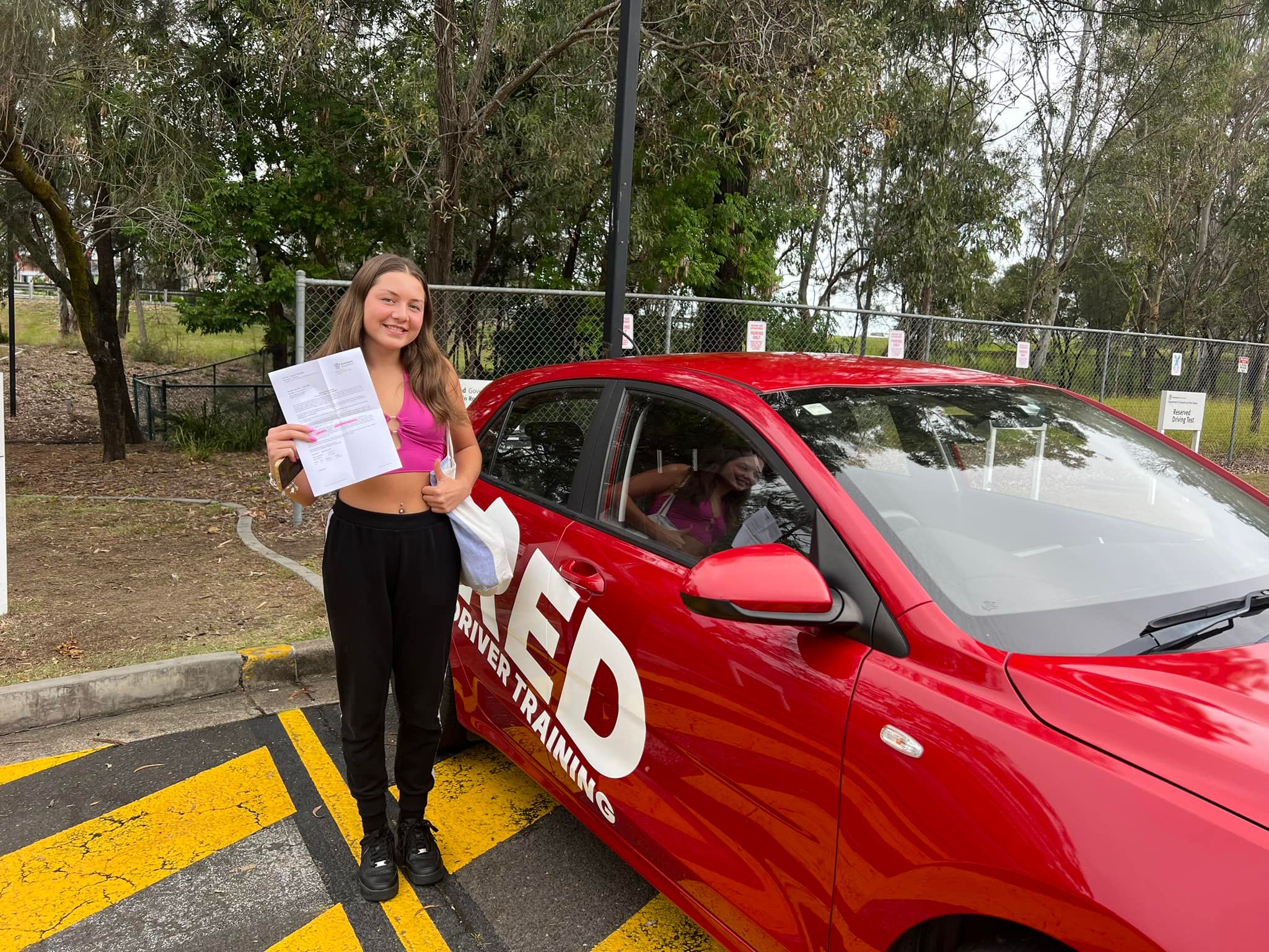 Student posing next to RED Driver Training dual-control vehicle after passing driving test on the Gold Coast