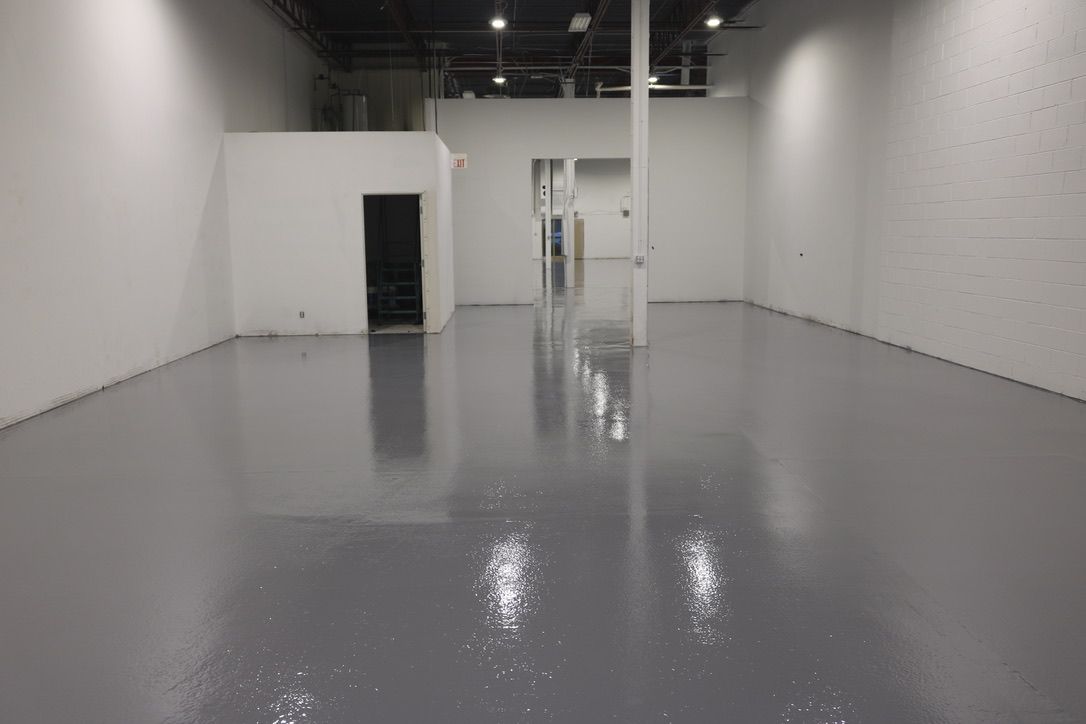 Large empty manufacturing space with smooth shiny grey epoxy floor, white pillar and exposed ceiling beams