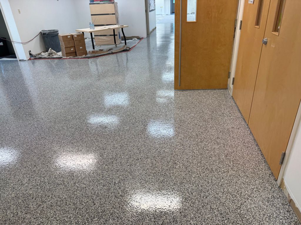 School hallway with shiny speckled gray epoxy floor, classroom doors and renovation equipment along wall