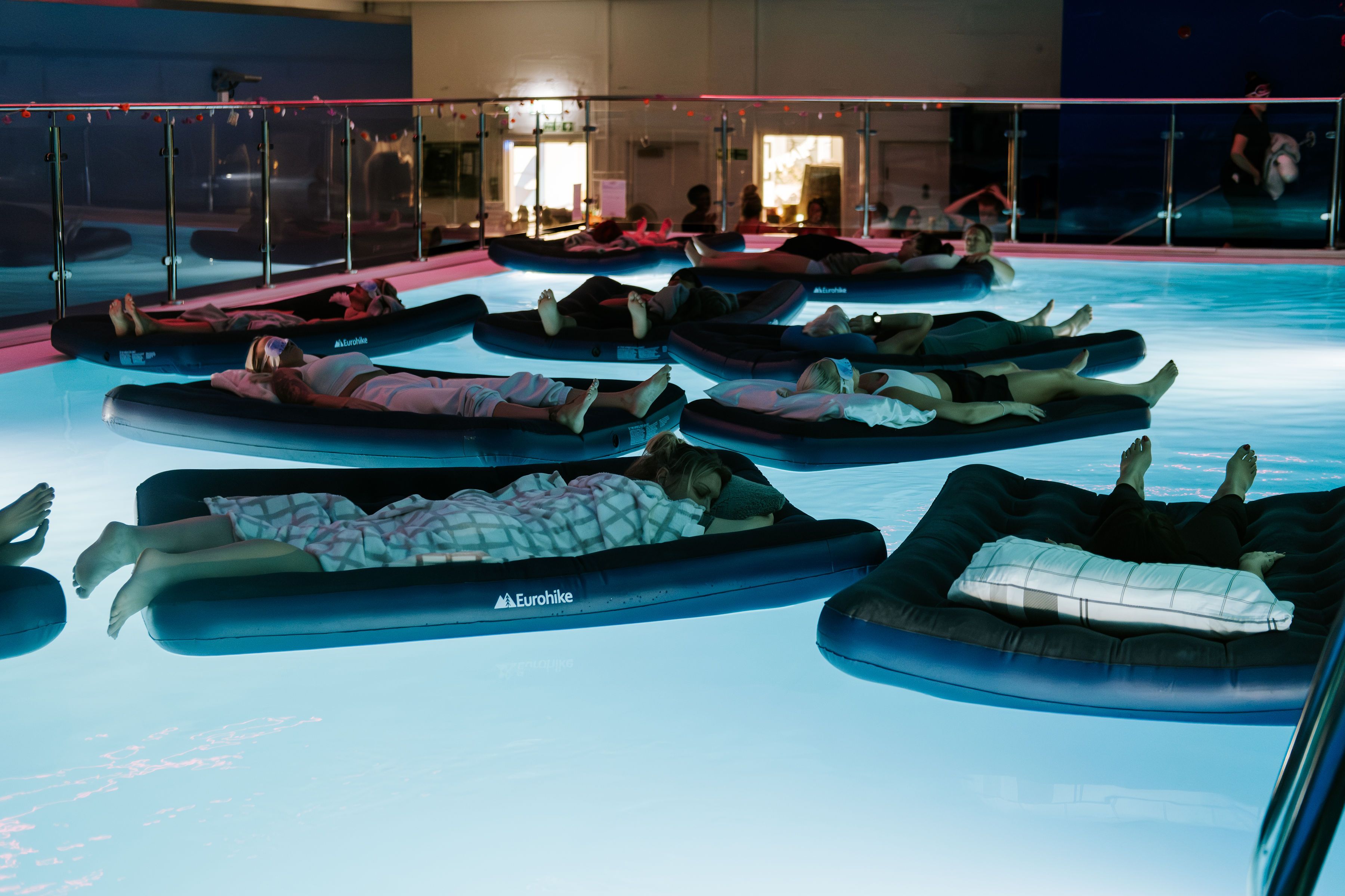 People resting on floating mats in a pool at a floating sound bath