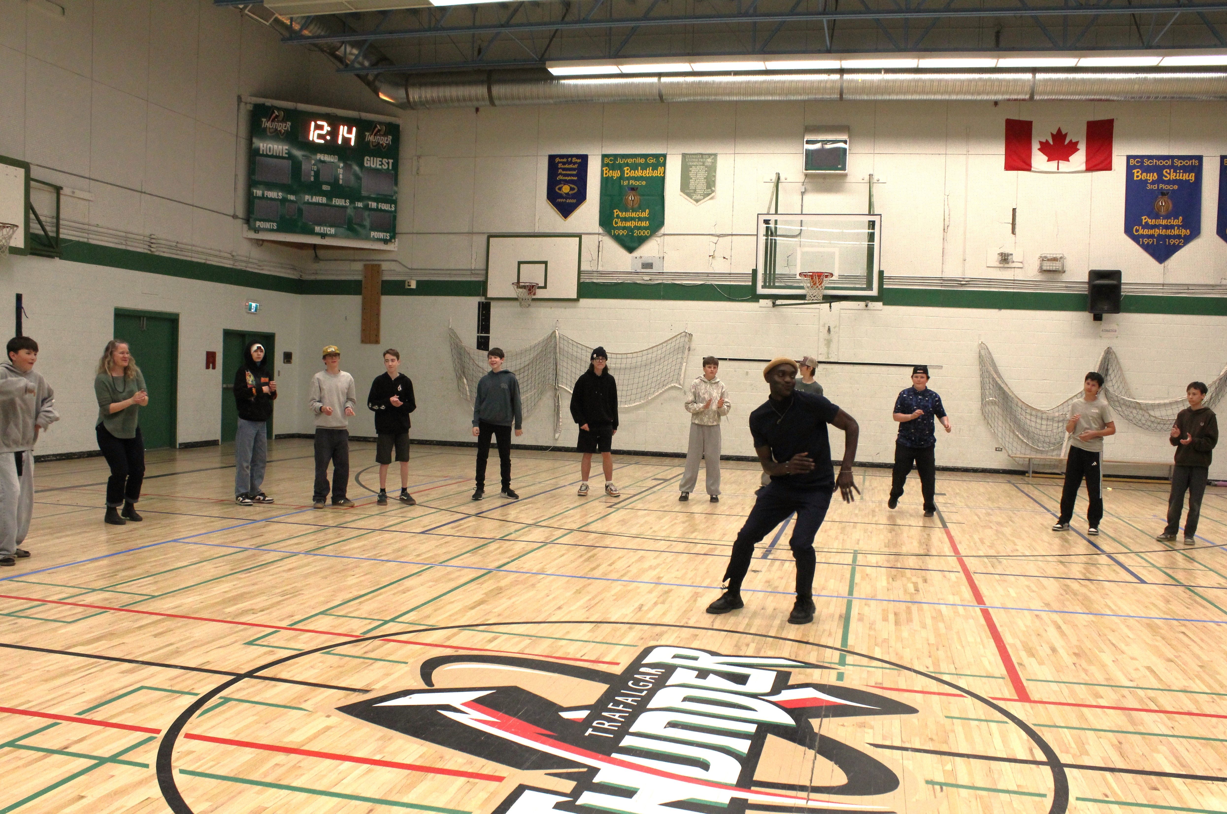Students forming a semi-circle around the facilitator during a rhythm exercise in a gymnasium