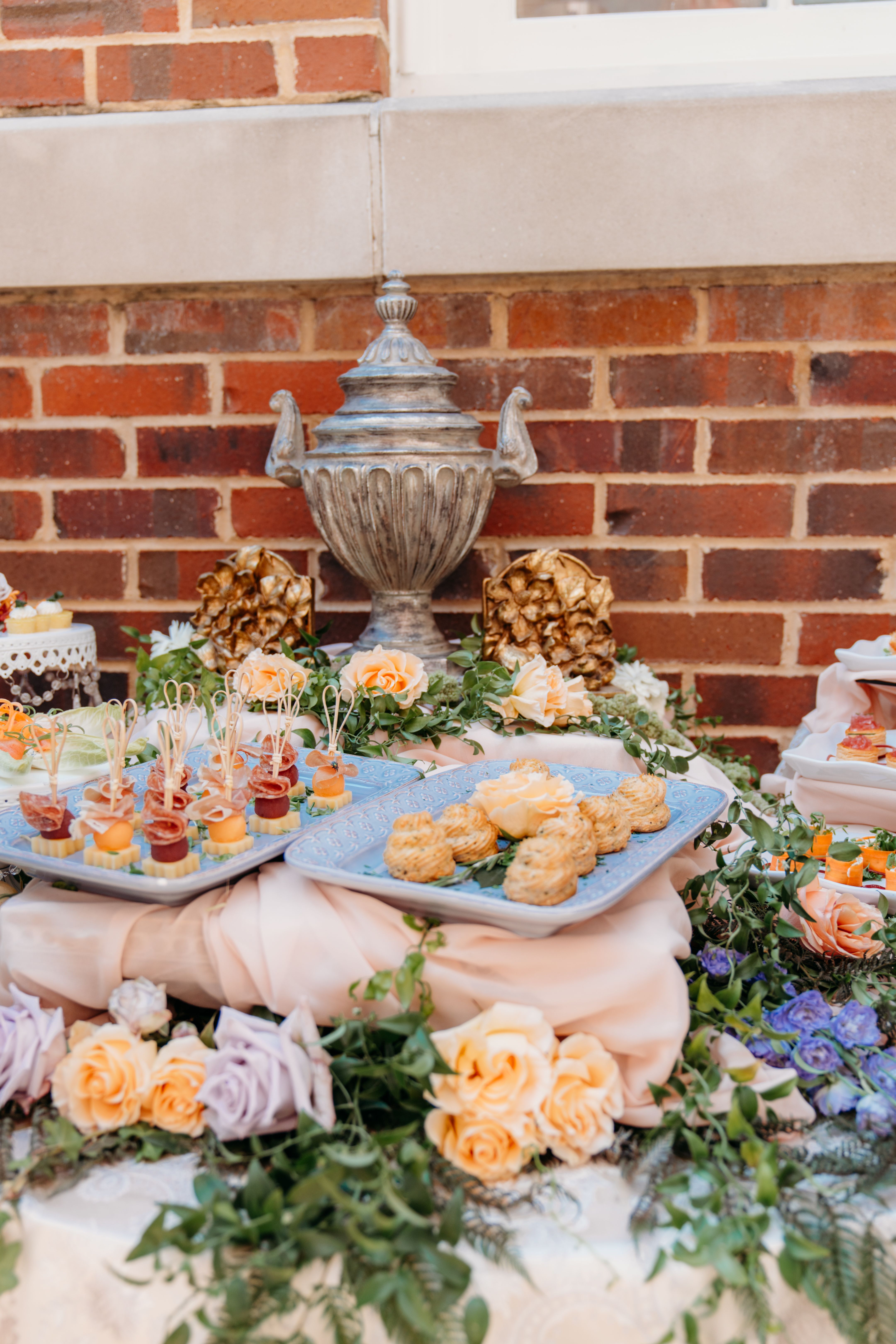 Styled food display with peach roses and lavender accents at a brick-walled venue