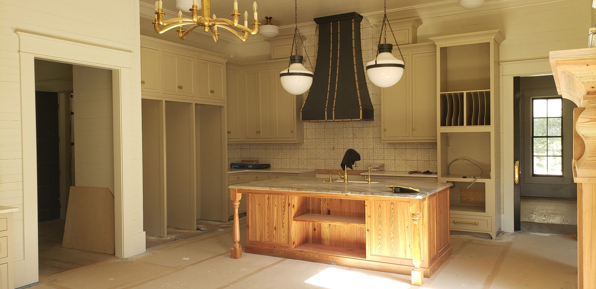 Kitchen under construction with gold chandelier and custom cabinetry