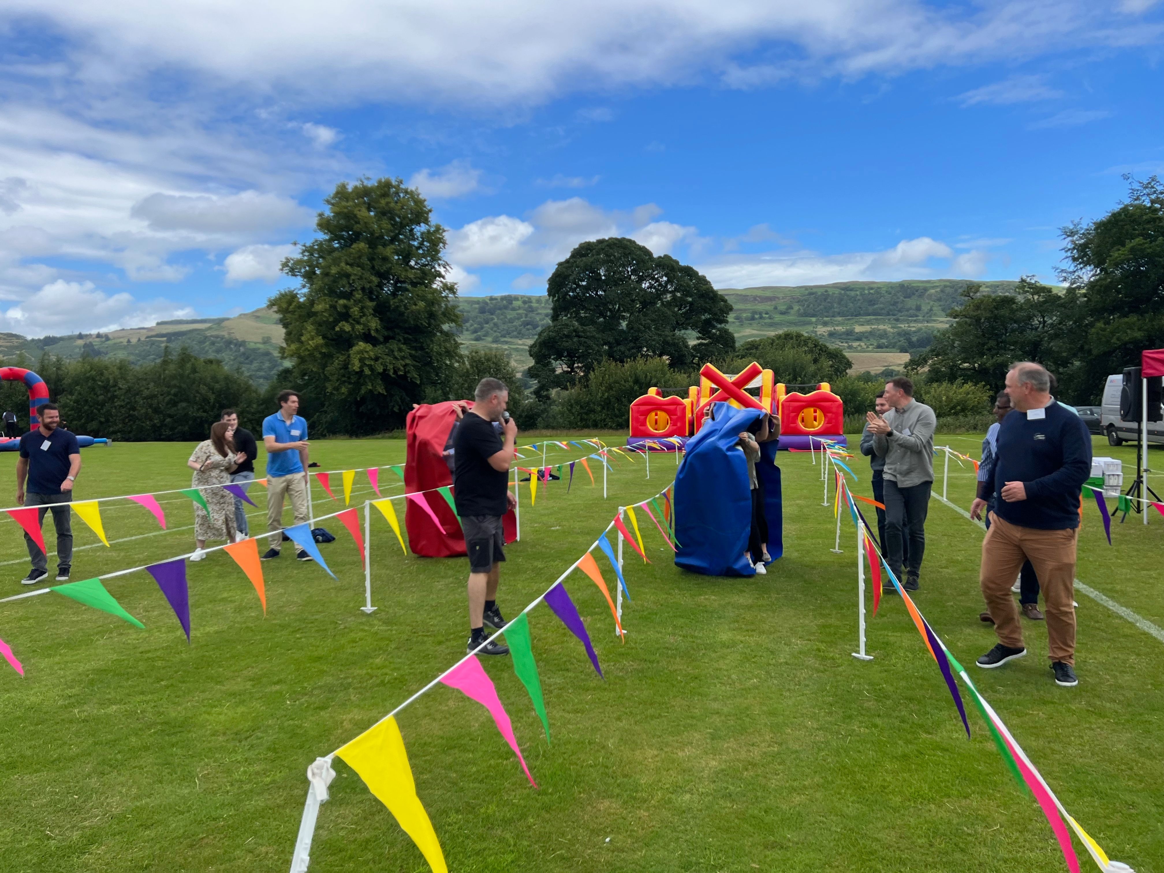 Participants in padded suits competing in an It's a Knockout challenge with bunting and roped arena