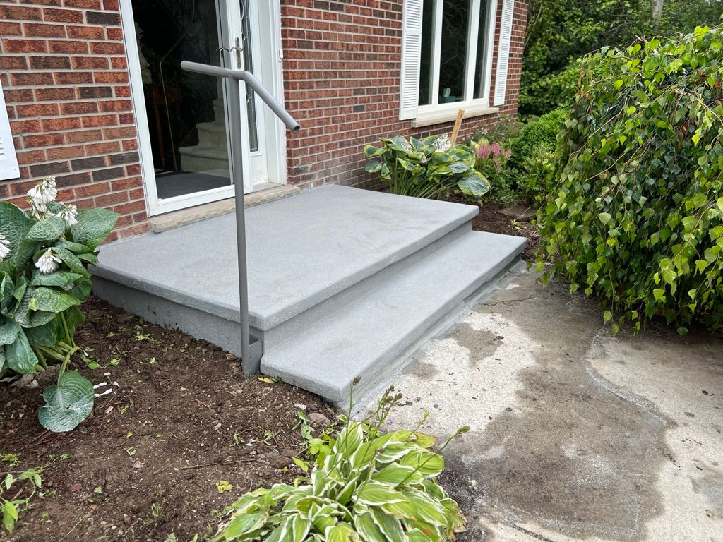 Small concrete porch with two steps leading to brick house before polymer coating application — metal handrail and garden