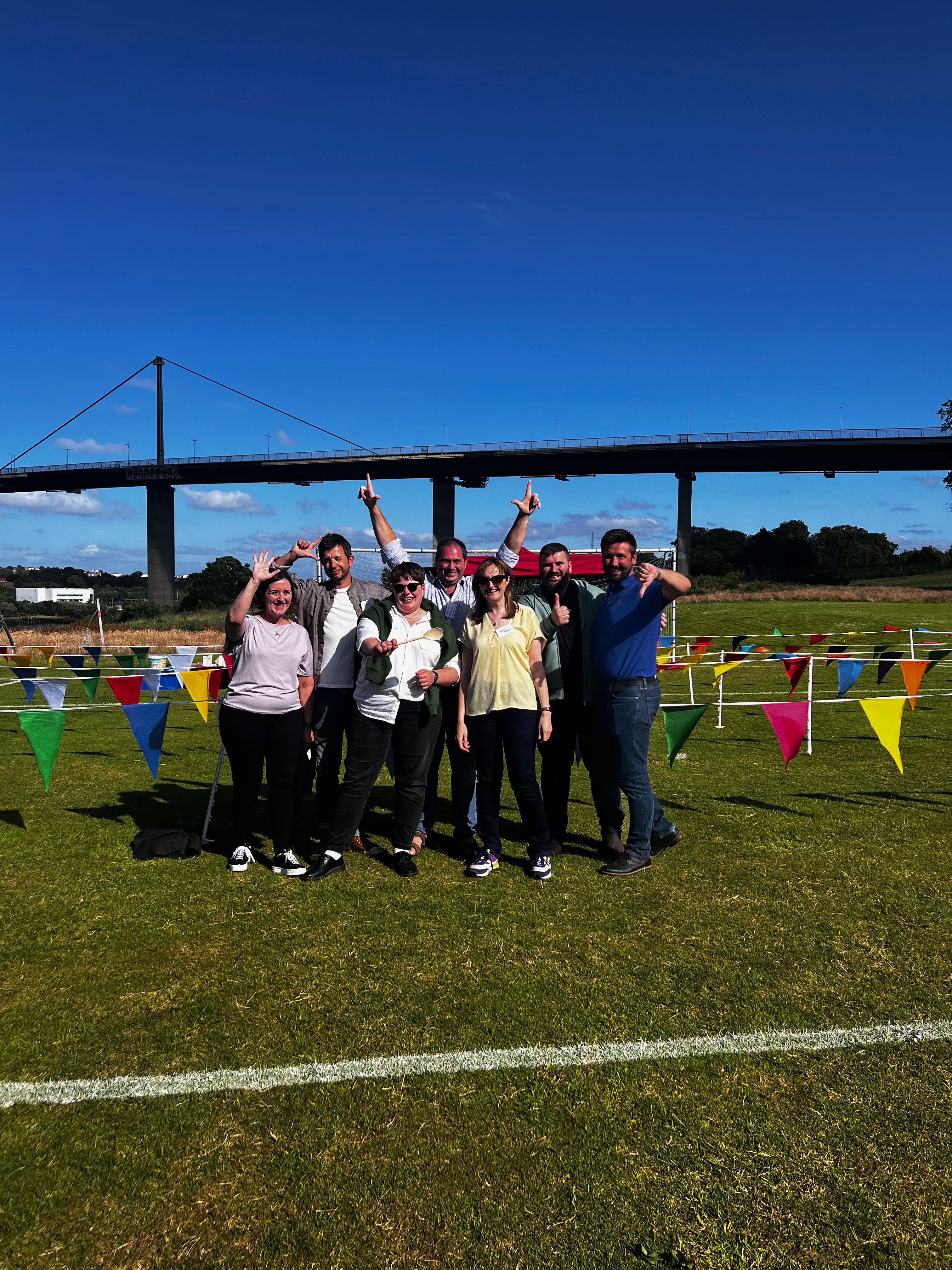 Seven smiling team members celebrating after It's a Knockout corporate fun day with bunting