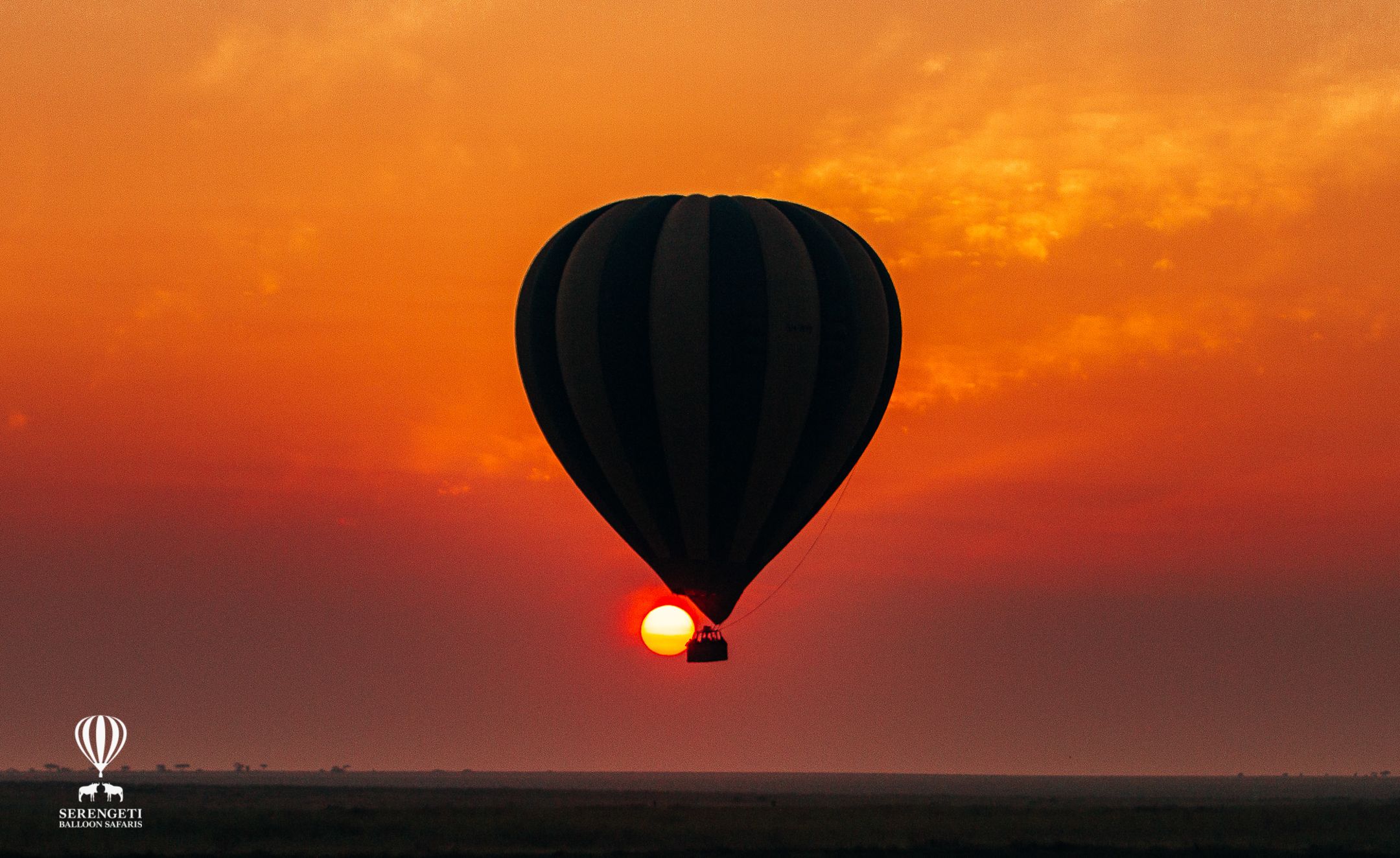 Hot air balloon silhouetted against a vibrant sunset over the Serengeti