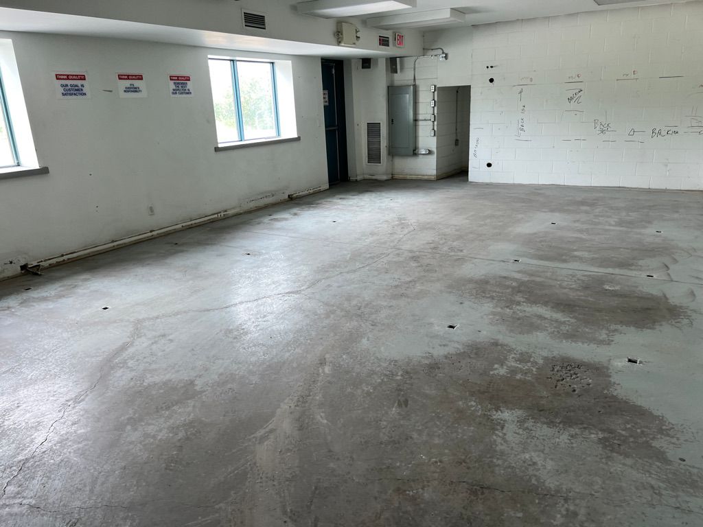 Empty high-tech space before installation — cracked concrete floor with white walls, windows, warning signs and fluorescent lighting