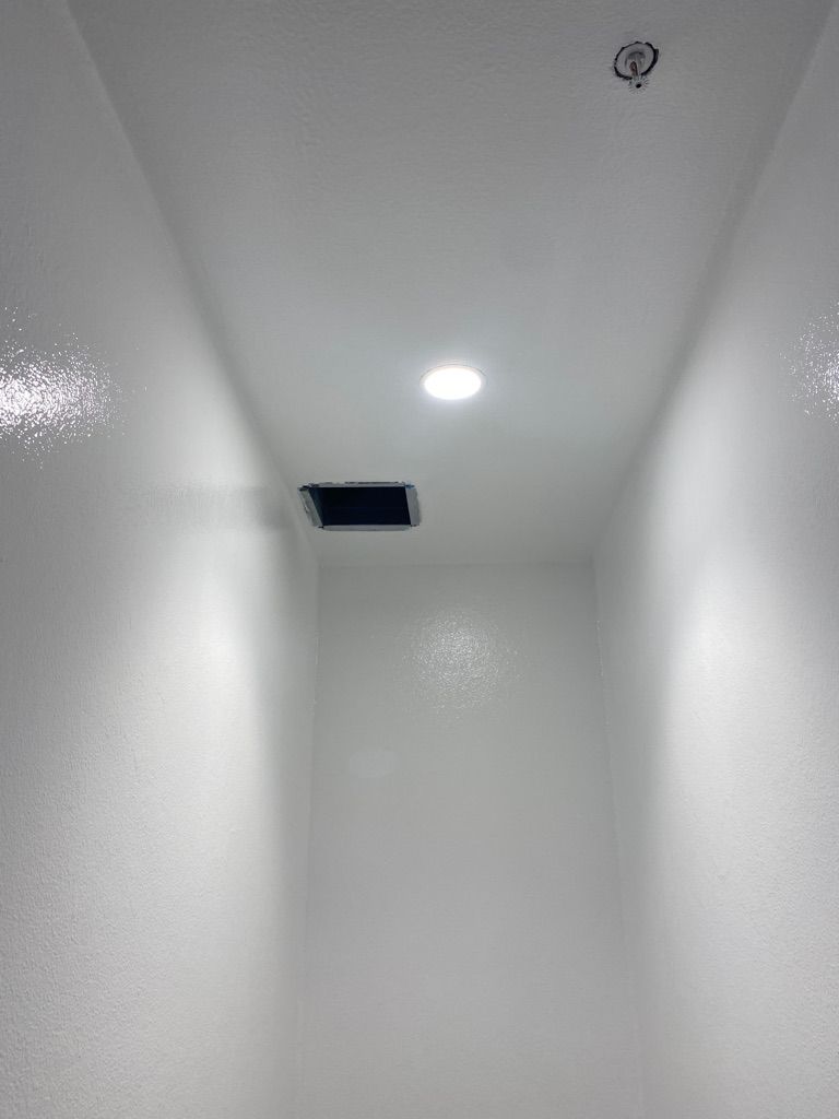 Clean pharmaceutical clean room or corridor with smooth white walls, active ceiling light and ventilation opening — post-installation view