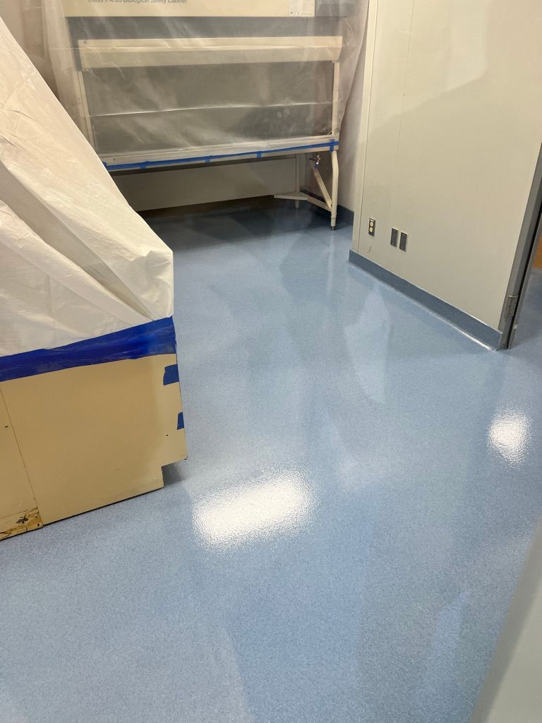 Pharmaceutical room with newly installed light blue seamless floor and large equipment covered with transparent protective plastic sheeting