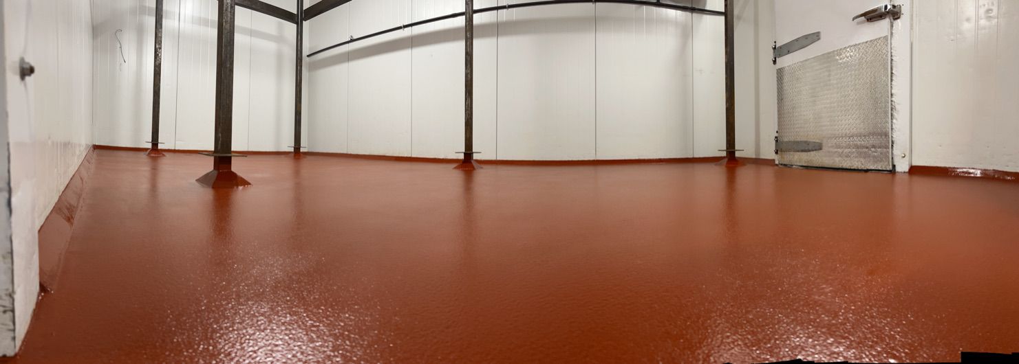 Empty food and beverage facility room with reddish-brown epoxy floor and structural support beams