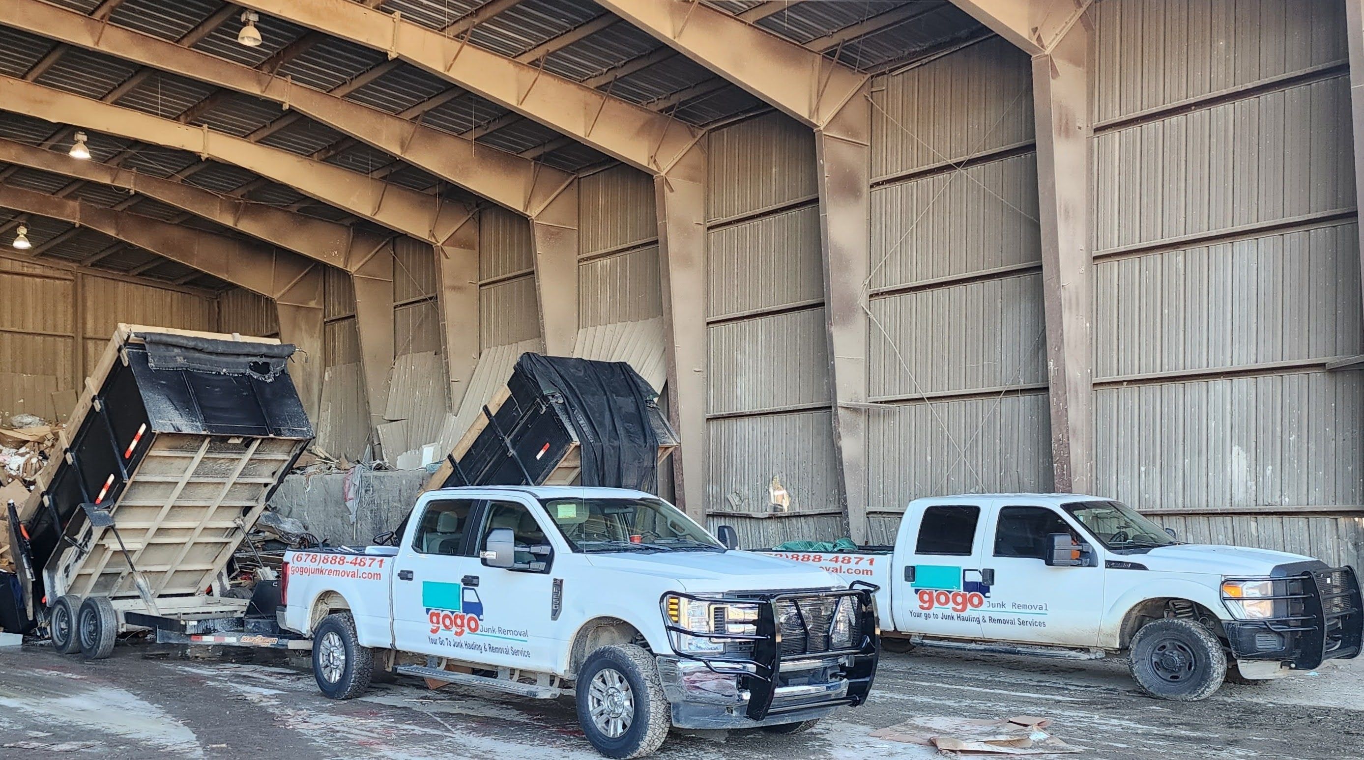 Two GoGo trucks at warehouse transfer station - GoGo Junk Removal fleet white pickups with trailers at disposal facility serving McDonough