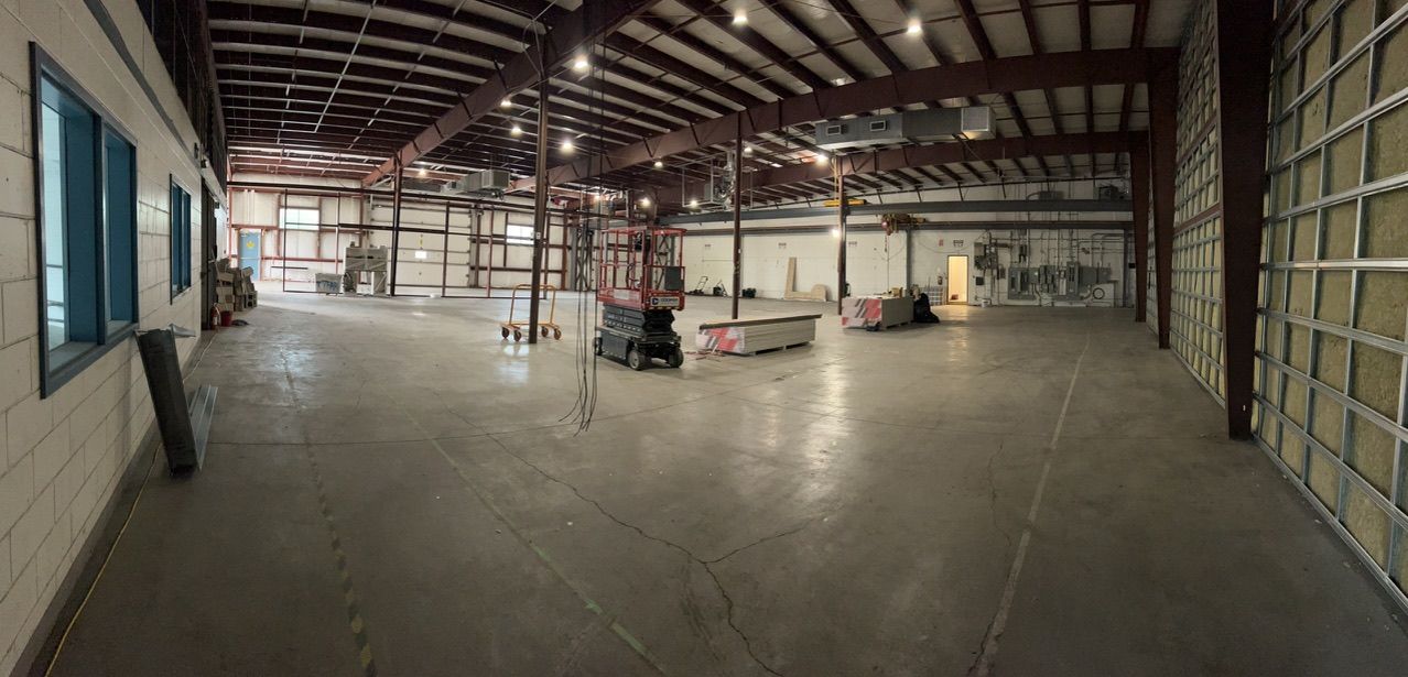 Large warehouse with concrete floor under assessment, metal beams, red scissor lift in center and electrical panels on far wall