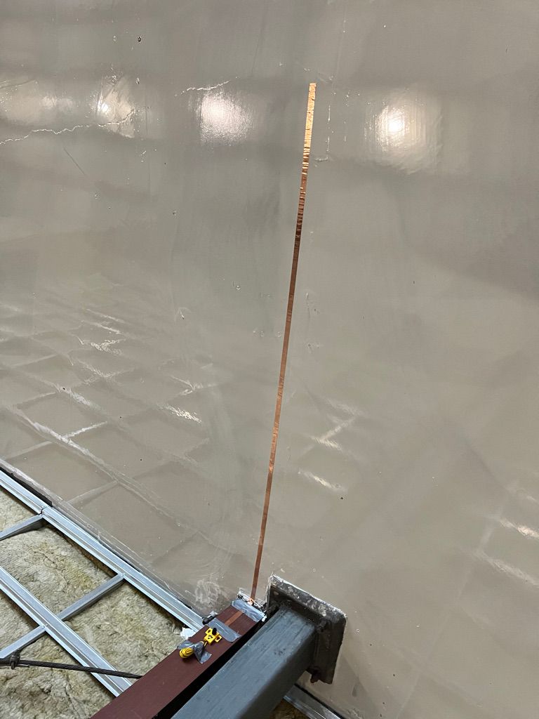 Close-up corner with copper ESD grounding strip on vertical beam, metal bracket at floor level and insulation framing