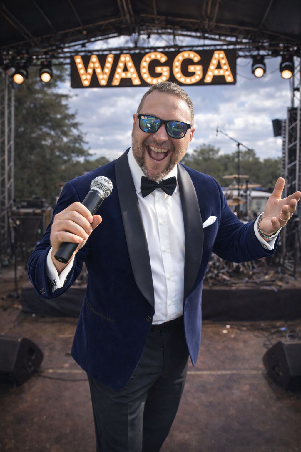 WAGGA in blue velvet tuxedo with microphone and WAGGA sign lit up behind