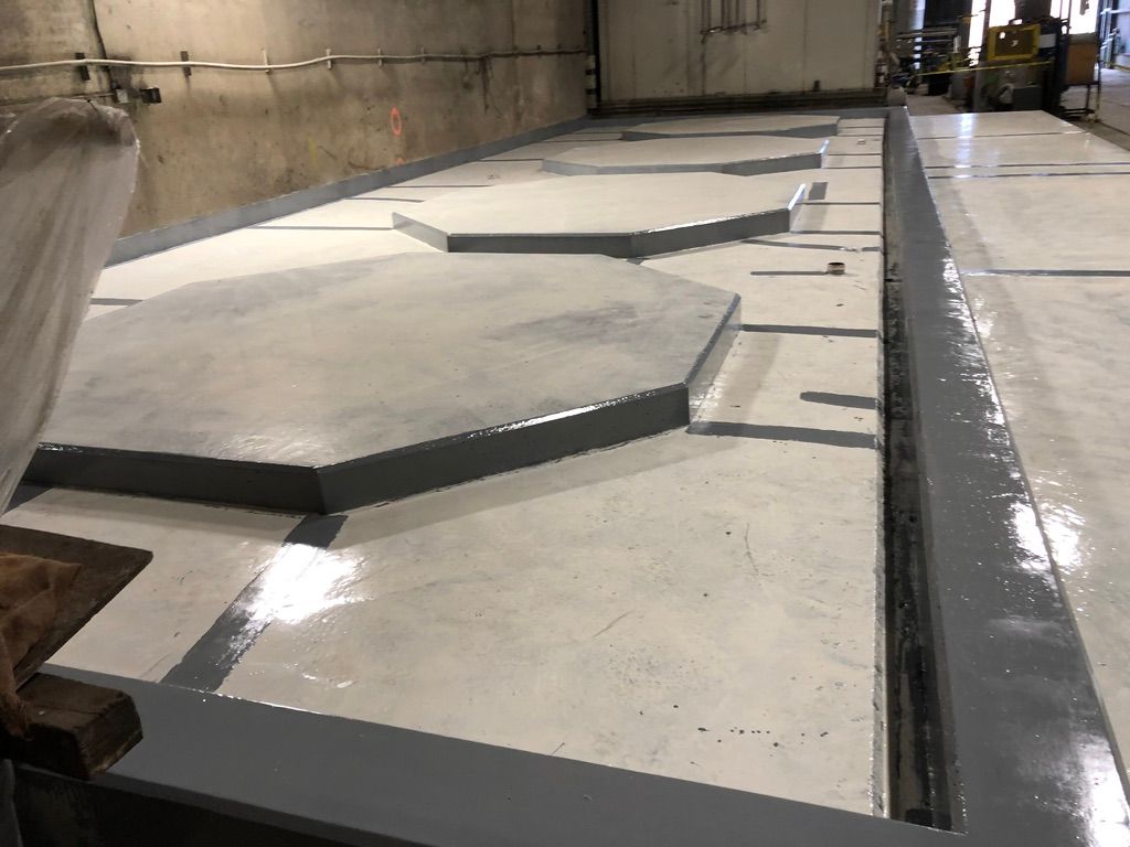 Row of raised octagonal platforms coated in seamless grey epoxy aligned across a glossy-finished water treatment facility floor under industrial overhead lighting