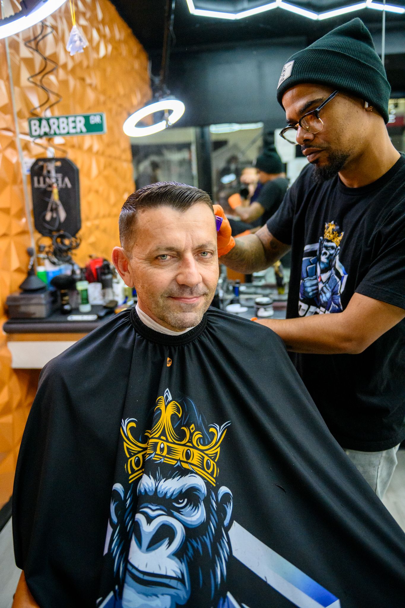 Barber styling client's hair with Gorilla Grooming branding on wall