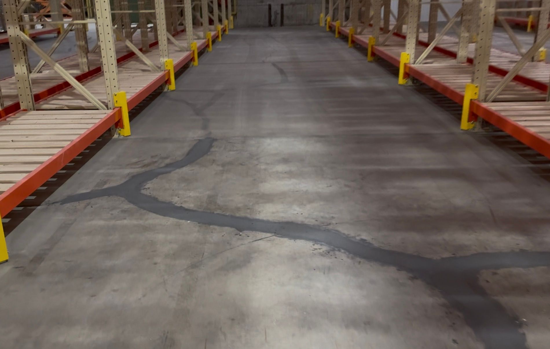 Warehouse aisle before-shot showing cracked and deteriorated concrete floor alongside empty red shelving