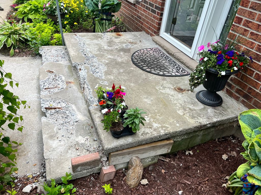 Weathered concrete front porch steps with cracked and stained surface before repair — brick wall entrance with flower pots