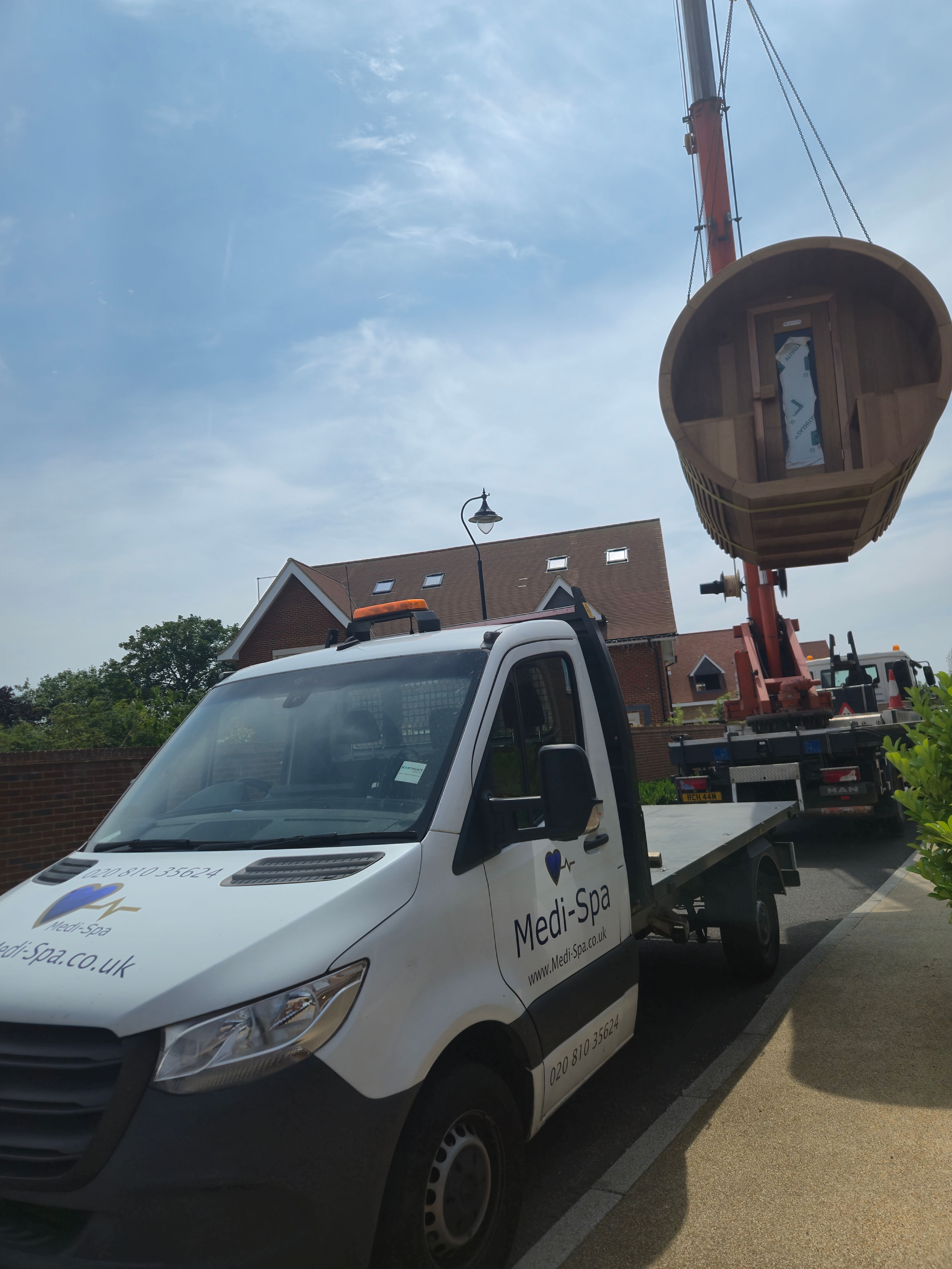 Medi-Spa truck and crane lifting a hot tub on a residential street