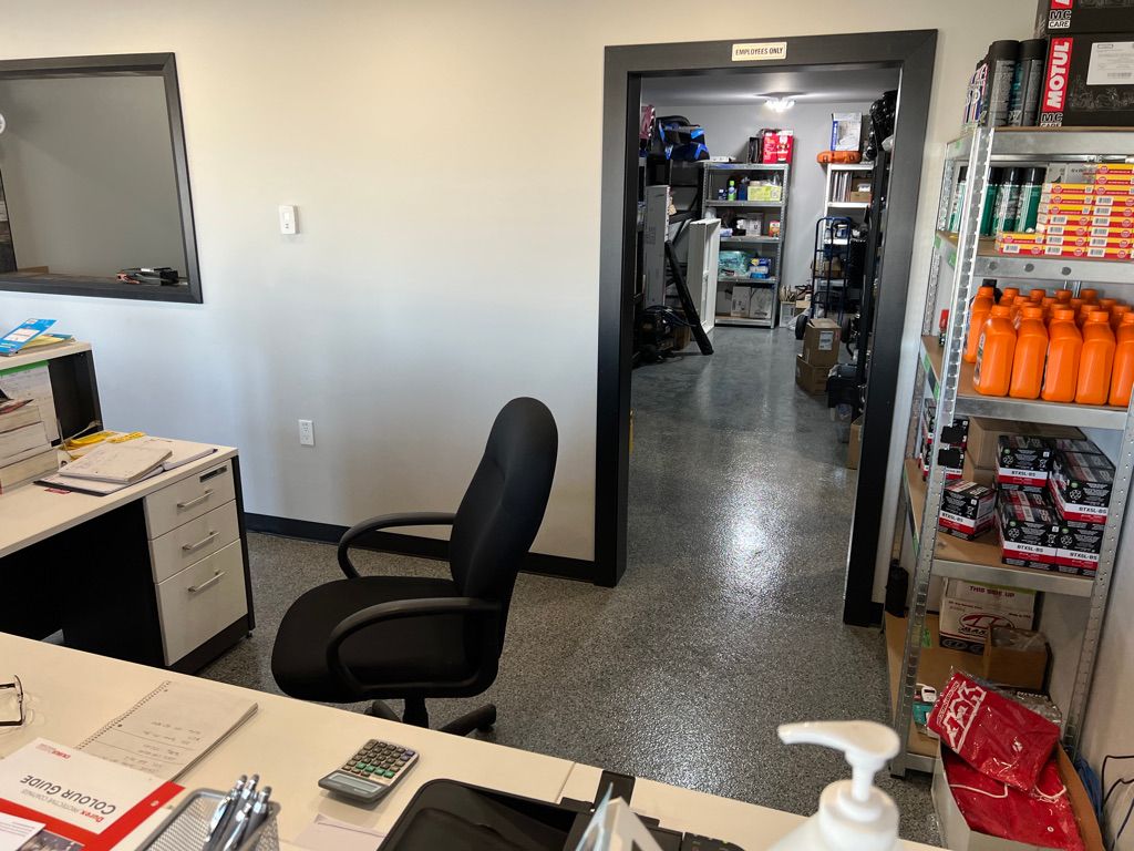 Retail back office area with desk, colour guide book and metal shelving stocked with products — employees only storage room beyond